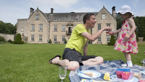 Family having a picnic in the gardens by the south front of the house at Nunnington Hall, North Yorkshire in June